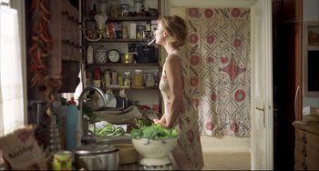 Movie still from “Funny Games” (1997), directed by Michael Haneke – A woman standing in a kitchen preparing a meal; Medium shot, Over the shoulder angle