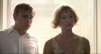 Movie still from “Funny Games” (1997), directed by Michael Haneke – A woman standing next to a young man in front of a window; Close Up shot, Low angle