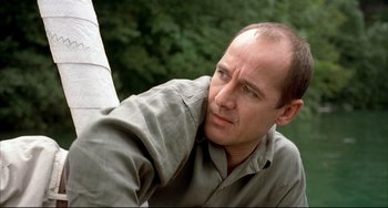 Movie still from “Funny Games” (1997), directed by Michael Haneke – A man with a bald head is leaning against a wall; Close Up shot, Low angle