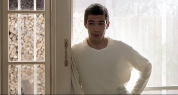 Movie still from “Funny Games” (1997), directed by Michael Haneke – A young man standing in front of a door; Medium shot, Over the shoulder angle