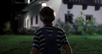 Movie still from “Funny Games” (1997), directed by Michael Haneke – A young boy standing in front of a house at night; Wide shot, Over the shoulder angle