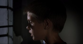 Movie still from “Funny Games” (1997), directed by Michael Haneke – A young man with a short haircut is looking into the light; Close Up shot, Low angle