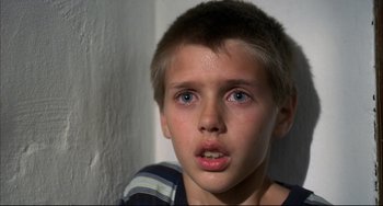 Movie still from “Funny Games” (1997), directed by Michael Haneke – A young boy with blue eyes stares into the camera; Close Up shot, High angle