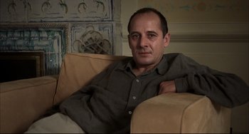 Movie still from “Funny Games” (1997), directed by Michael Haneke – A man sitting on a couch with his arm resting on his chest; Close Up shot, Low angle