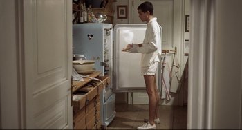 Movie still from “Funny Games” (1997), directed by Michael Haneke – A man standing in front of an open refrigerator in a kitchen; Wide shot, Low angle