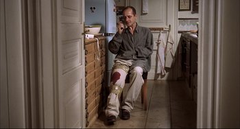Movie still from “Funny Games” (1997), directed by Michael Haneke – A man sitting on a chair in a room; Wide shot, High angle