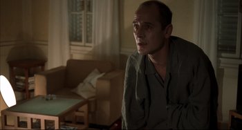 Movie still from “Funny Games” (1997), directed by Michael Haneke – A man sitting on a couch in a living room; Medium shot, Low angle