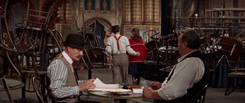Movie still from “Funny Girl” (1968), directed by William Wyler – A man sitting at a table writing on a piece of paper; Wide shot, High angle