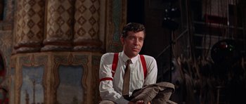 Movie still from “Funny Girl” (1968), directed by William Wyler – A man wearing a tie and suspenders sitting on a chair; Medium shot, Low angle