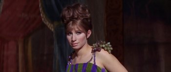 Movie still from “Funny Girl” (1968), directed by William Wyler – A woman in a purple and green striped dress with a bunch of grapes in her hair; Close Up shot, Low angle