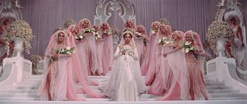 Movie still from “Funny Girl” (1968), directed by William Wyler – A woman in a wedding dress standing in front of a group of women in pink dresses; Wide shot, High angle