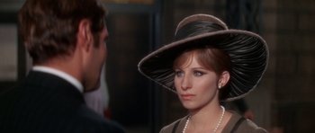 Movie still from “Funny Girl” (1968), directed by William Wyler – A woman wearing a hat and a pearl necklace looks at a man; Close Up shot, Over the shoulder angle