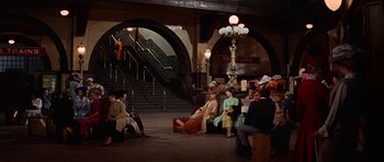 Movie still from “Funny Girl” (1968), directed by William Wyler – A group of people sitting on a bench in a train station; Wide shot, High angle