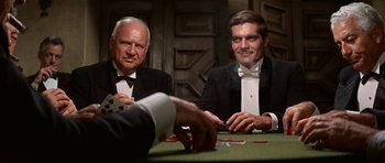 Movie still from “Funny Girl” (1968), directed by William Wyler – Two men sitting at a table with cards in front of them; Medium shot, Over the shoulder angle