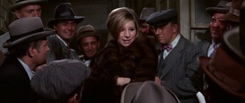 Movie still from “Funny Girl” (1968), directed by William Wyler – A woman in a fur coat surrounded by men in hats; Medium shot, Over the shoulder angle