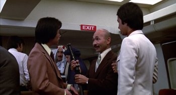 Movie still from “Futureworld” (1976), directed by Richard T. Heffron – A group of men standing around talking to each other in front of a exit sign; Medium shot, Over the shoulder angle