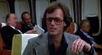 Movie still from “Futureworld” (1976), directed by Richard T. Heffron – A man in a suit and glasses is sitting on a plane; Close Up shot, Over the shoulder angle