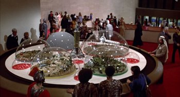 Movie still from “Futureworld” (1976), directed by Richard T. Heffron – A group of people standing around a table with food on top of it; Extreme Wide shot, High angle