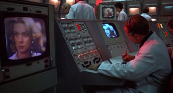 Movie still from “Futureworld” (1976), directed by Richard T. Heffron – A person is sitting at a control panel in front of a television; Medium shot, Over the shoulder angle