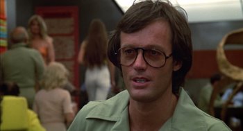 Movie still from “Futureworld” (1976), directed by Richard T. Heffron – A person wearing glasses with people in the background; Close Up shot, Over the shoulder angle