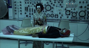 Movie still from “Futureworld” (1976), directed by Richard T. Heffron – A woman standing in front of a man laying on a table; Medium shot, Low angle