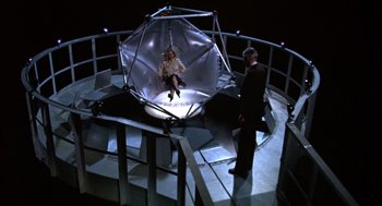 Movie still from “Futureworld” (1976), directed by Richard T. Heffron – A woman sitting in an enclosed space with a man standing next to it; Wide shot, High angle
