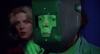 Movie still from “Futureworld” (1976), directed by Richard T. Heffron – A person wearing a green mask and a woman looking on; Close Up shot, Over the shoulder angle