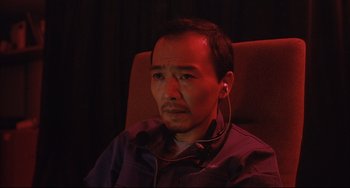 Movie still from “Gamera 3: Revenge of Iris” (1999), directed by Shûsuke Kaneko – A man sitting in a chair wearing headphones; Close Up shot, High angle