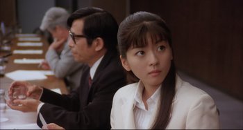 Movie still from “Gamera 3: Revenge of Iris” (1999), directed by Shûsuke Kaneko – A woman in a white jacket sitting in front of a man; Close Up shot, Over the shoulder angle