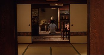 Movie still from “Gamera 3: Revenge of Iris” (1999), directed by Shûsuke Kaneko – An older woman sitting on the ground in a room; Wide shot, Over the shoulder angle