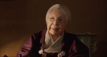 Movie still from “Gamera 3: Revenge of Iris” (1999), directed by Shûsuke Kaneko – An older woman wearing glasses and a purple jacket; Close Up shot, Low angle