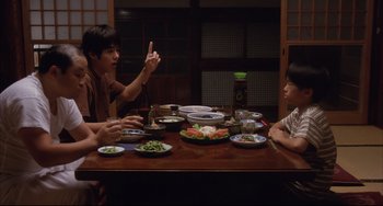 Movie still from “Gamera 3: Revenge of Iris” (1999), directed by Shûsuke Kaneko – Two people sitting at a table with plates of food on it; Medium shot, Over the shoulder angle