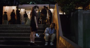 Movie still from “Gamera 3: Revenge of Iris” (1999), directed by Shûsuke Kaneko – A man sitting on the ground next to a woman on the stairs; Wide shot, Low angle