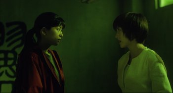 Movie still from “Gamera 3: Revenge of Iris” (1999), directed by Shûsuke Kaneko – Two women standing next to each other in a green room; Medium shot, Over the shoulder angle