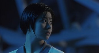 Movie still from “Gamera 3: Revenge of Iris” (1999), directed by Shûsuke Kaneko – A woman with short black hair is looking into the distance; Close Up shot, Low angle