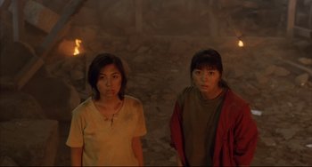 Movie still from “Gamera 3: Revenge of Iris” (1999), directed by Shûsuke Kaneko – Two young women standing next to each other in front of a fire pit; Medium shot, High angle