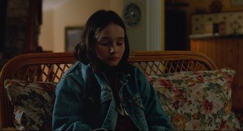 Movie still from “Aftersun” (2022), directed by Charlotte Wells – A young girl sitting on a wicker couch; Medium shot, High angle