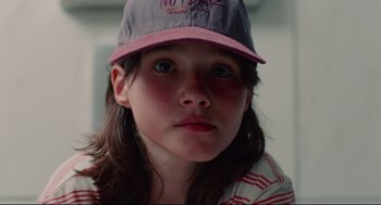 Movie still from “Aftersun” (2022), directed by Charlotte Wells – A young girl wearing a baseball cap and looking into the camera; Close Up shot, Low angle