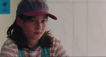 Movie still from “Aftersun” (2022), directed by Charlotte Wells – A young girl wearing a hat and a striped shirt; Close Up shot, High angle
