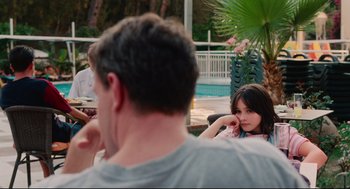 Movie still from “Aftersun” (2022), directed by Charlotte Wells – A young girl sitting next to an older man in front of a swimming pool; Medium shot, Over the shoulder angle