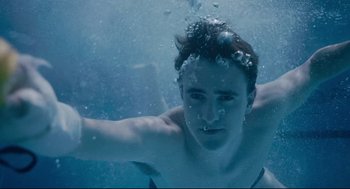 Movie still from “Aftersun” (2022), directed by Charlotte Wells – A man swimming underwater in a pool of water; Close Up shot, Overhead angle