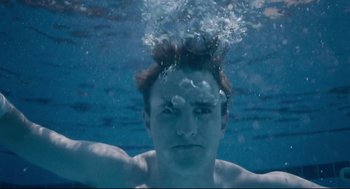 Movie still from “Aftersun” (2022), directed by Charlotte Wells – A man swimming in a pool of water with his head above the water; Close Up shot, Low angle