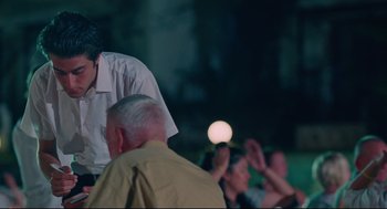 Movie still from “Aftersun” (2022), directed by Charlotte Wells – A group of people sitting in front of an audience at night; Medium shot, Over the shoulder angle