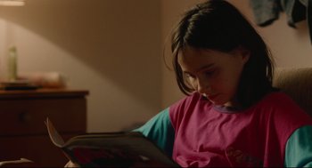 Movie still from “Aftersun” (2022), directed by Charlotte Wells – A young girl is reading a book in a room; Close Up shot, High angle