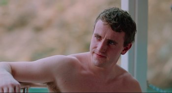 Movie still from “Aftersun” (2022), directed by Charlotte Wells – A man with a bare torso is looking at the camera; Close Up shot, Low angle