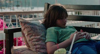Movie still from “Aftersun” (2022), directed by Charlotte Wells – A young girl sitting on top of a wooden bench; Medium shot, High angle
