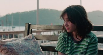 Movie still from “Aftersun” (2022), directed by Charlotte Wells – A young girl sitting on a wooden bench; Close Up shot, Over the shoulder angle