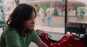 Movie still from “Aftersun” (2022), directed by Charlotte Wells – A young girl sitting next to a red motorcycle; Close Up shot, High angle