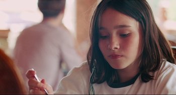 Movie still from “Aftersun” (2022), directed by Charlotte Wells – A young girl sitting at a table with a pen in her hand; Close Up shot, Over the shoulder angle