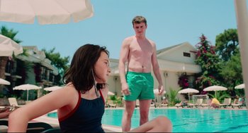 Movie still from “Aftersun” (2022), directed by Charlotte Wells – A man and a woman sitting in front of a swimming pool; Medium shot, Over the shoulder angle
